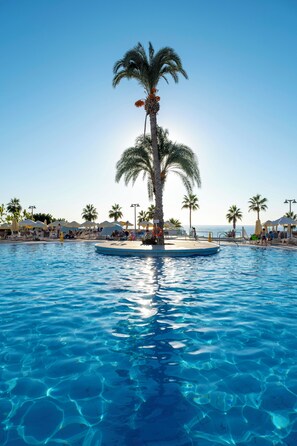 A clear blue pool with a palm tree in the center, surrounded by lounge chairs and umbrellas. - Leonardo Laura Beach & Splash Resort (Chlorakas)