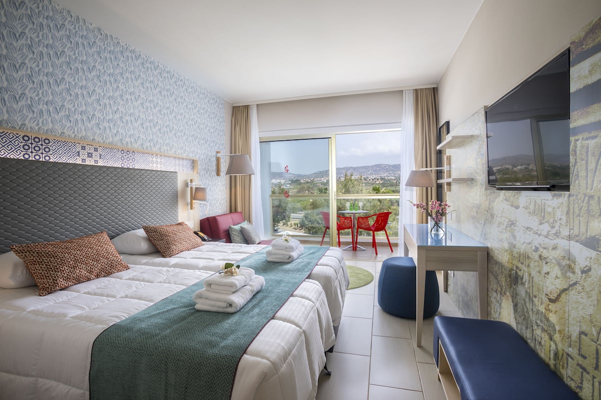 Une chambre d’hôtel avec un grand lit, un bureau, une télévision et un balcon avec vue.