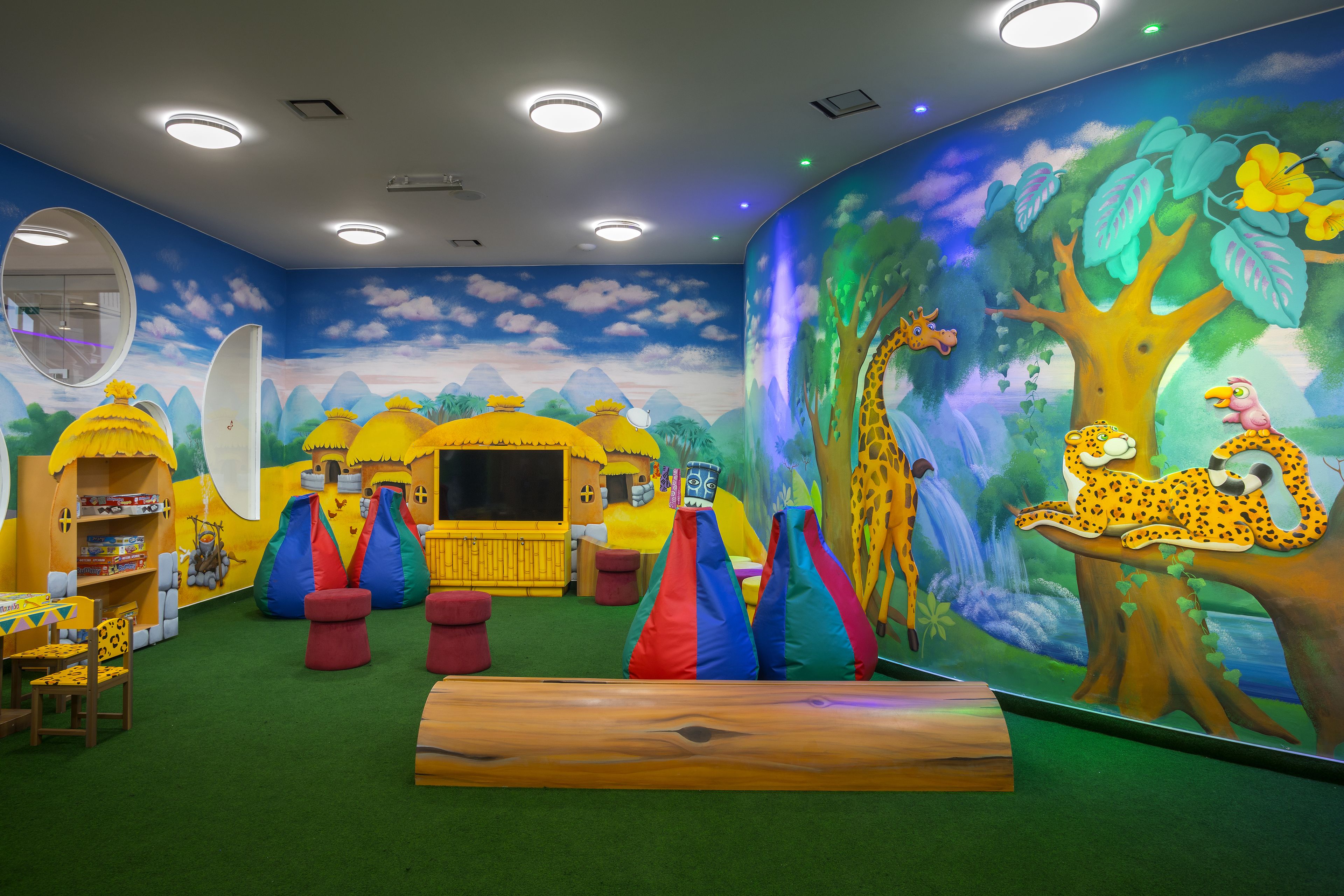 A children's playroom with a mural, play structures, and a wooden bench.