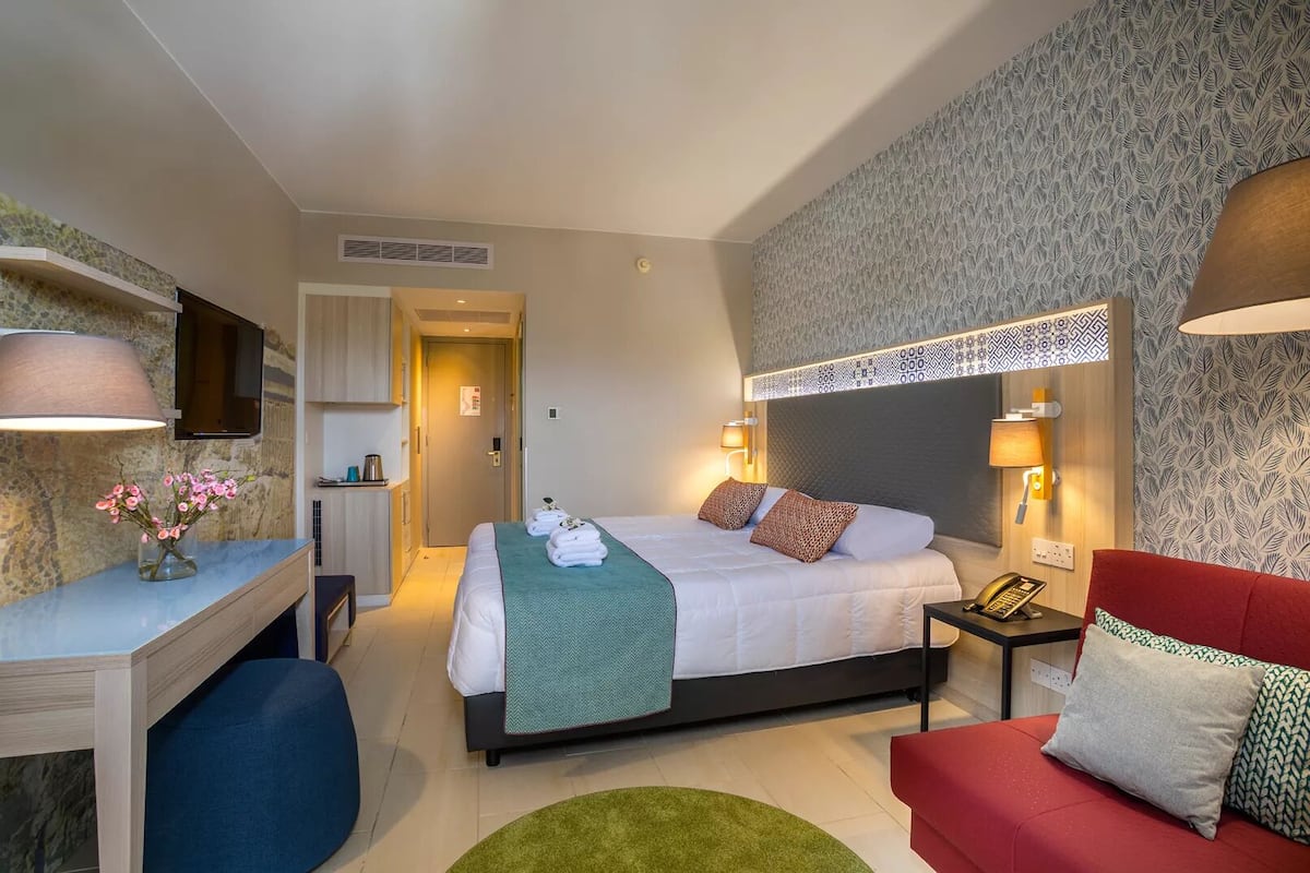Une chambre d’hôtel avec un lit, des tables de chevet, un bureau, un canapé rouge et un téléviseur.