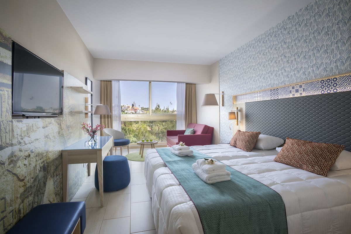 Une chambre d’hôtel avec un lit, un bureau, une chaise, une télévision et un balcon avec vue.