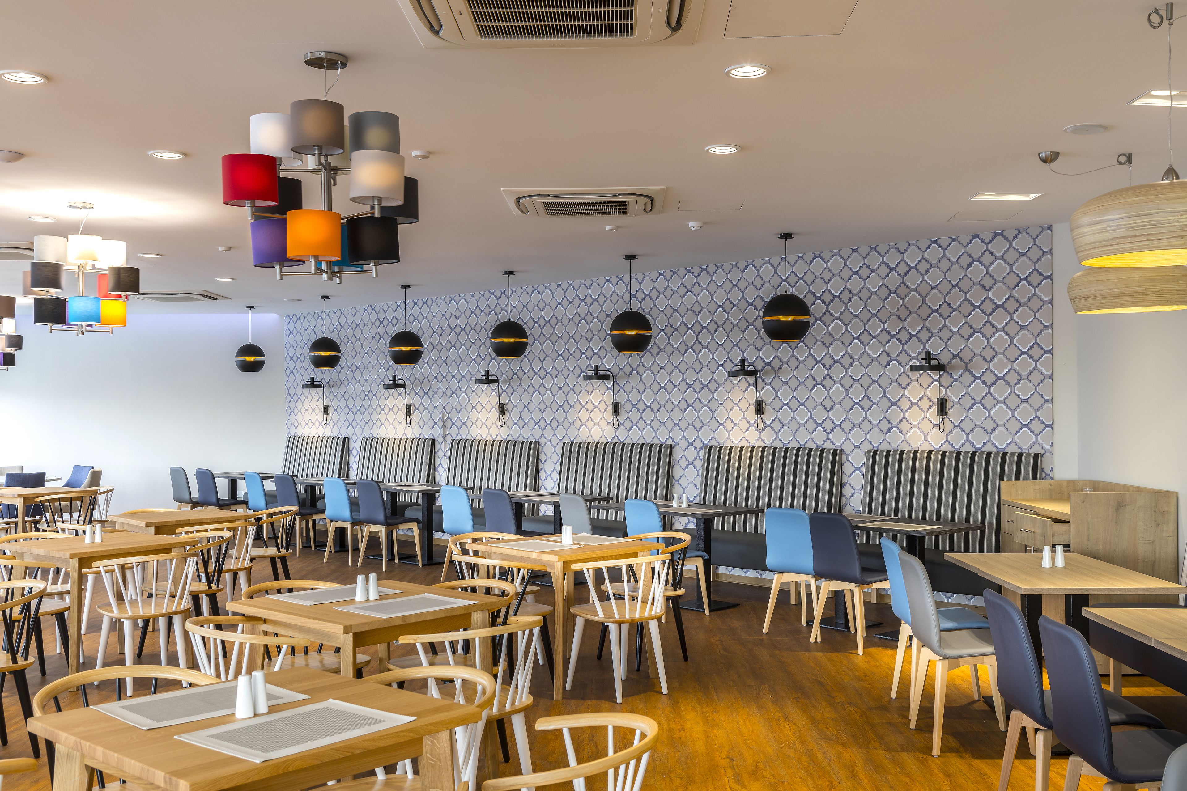 A modern restaurant with wooden tables and chairs, patterned wall tiles, and pendant lighting.