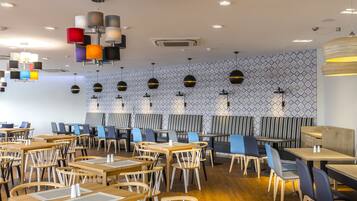A modern restaurant with wooden tables and chairs, patterned wall tiles, and pendant lighting.