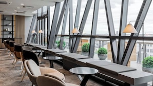 A modern lounge area with seating, tables, and large windows offering a view of the cityscape. - AC Hotel by Marriott Riga (Riga)