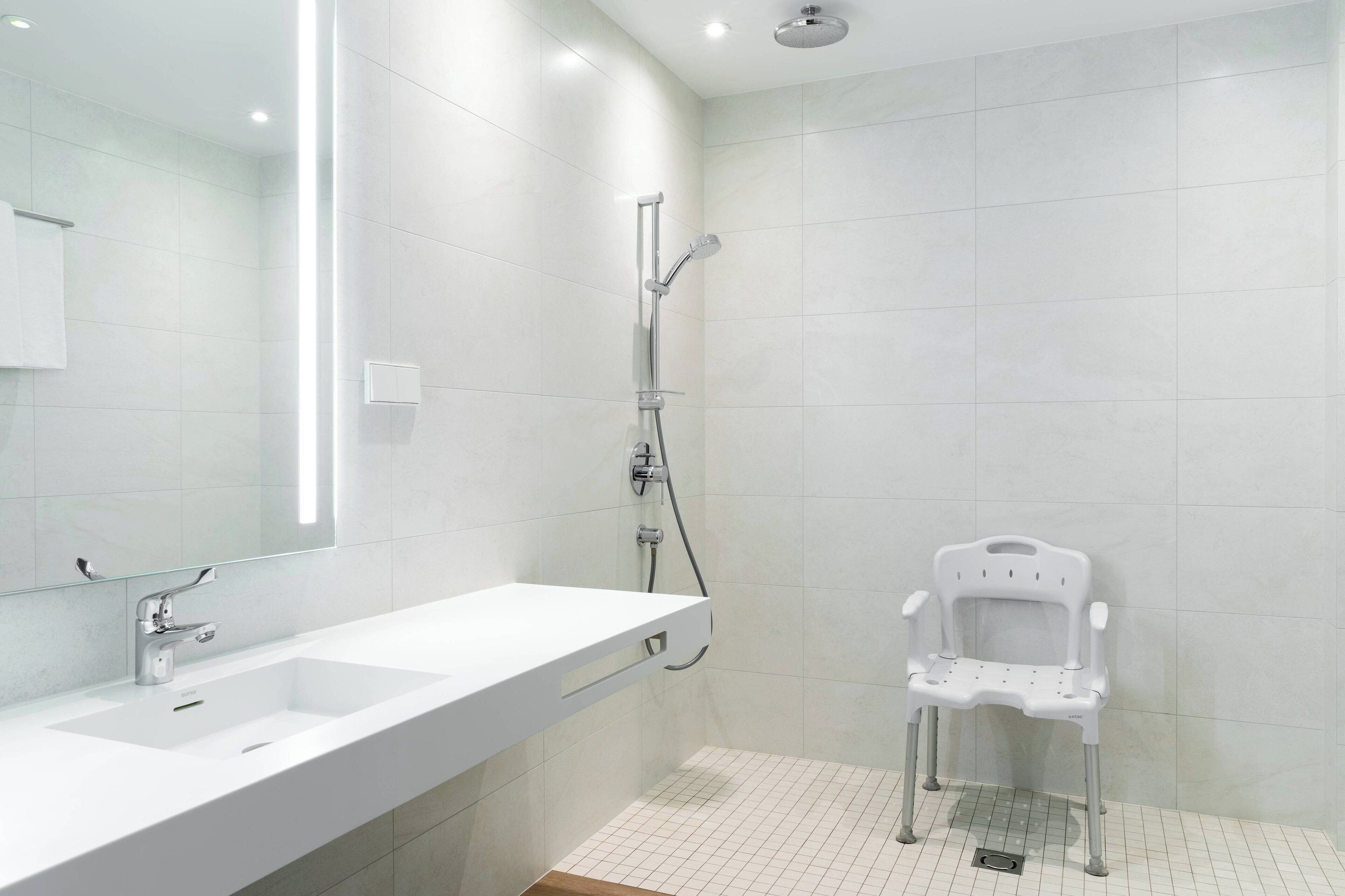 A modern bathroom with a white sink, a mirror, and a shower with a white chair.