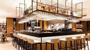 A bar area with a high bar counter, multiple stools, and a variety of bottles and glasses. - AC Hotel by Marriott Riga (Riga)