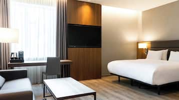 A hotel room with a bed, a desk, a chair, a TV, and a lamp.