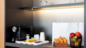 A breakfast setup with a coffee machine, croissants, fruits, and paper cups.