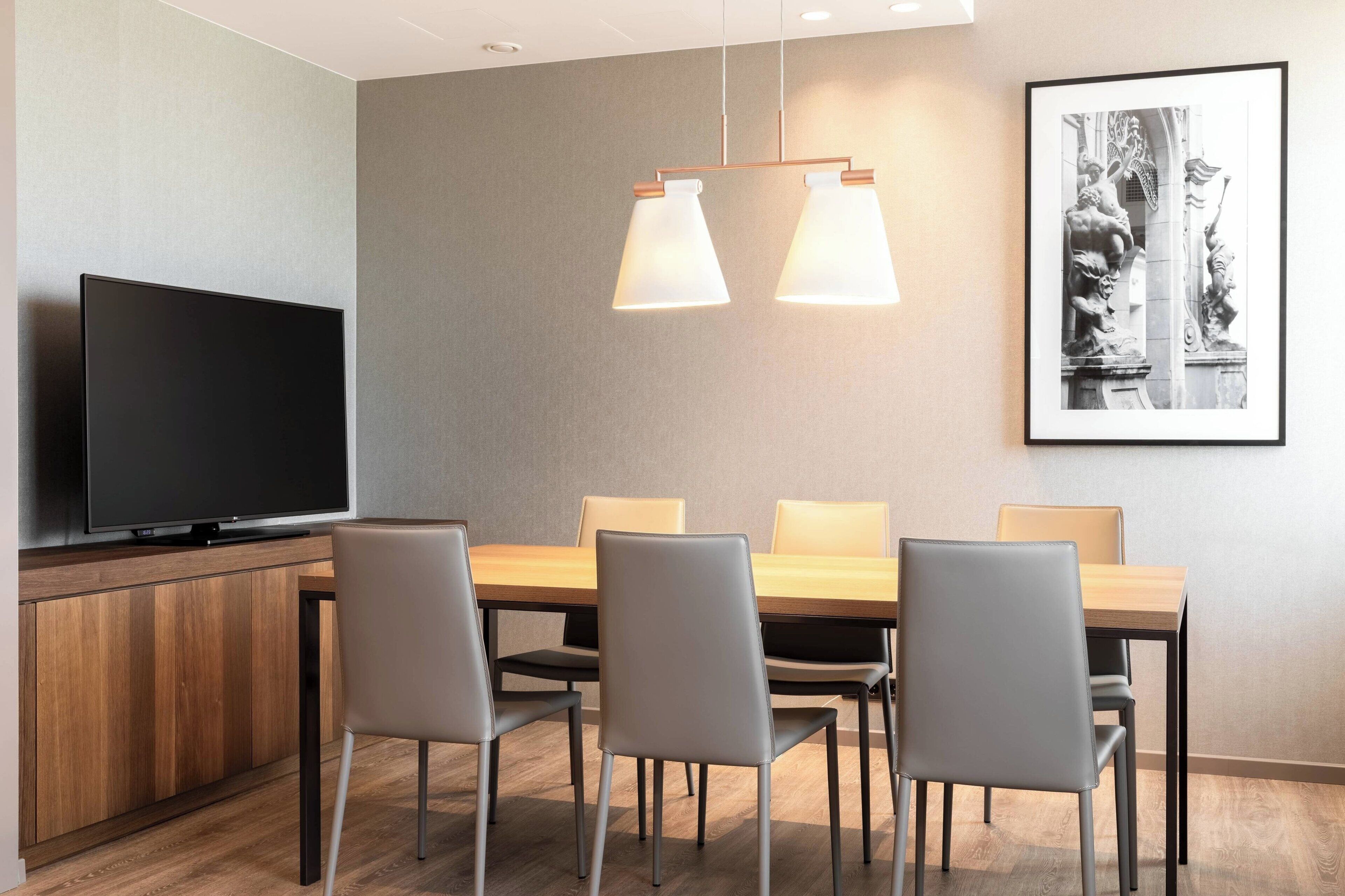 A modern dining area with a wooden table, six chairs, a flat-screen TV, and pendant lighting.