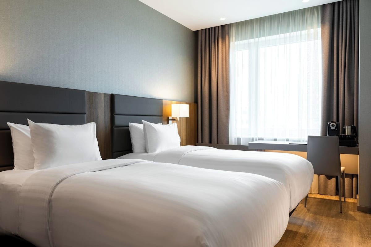 A hotel room with two beds, a desk, a chair, and a large window with curtains.