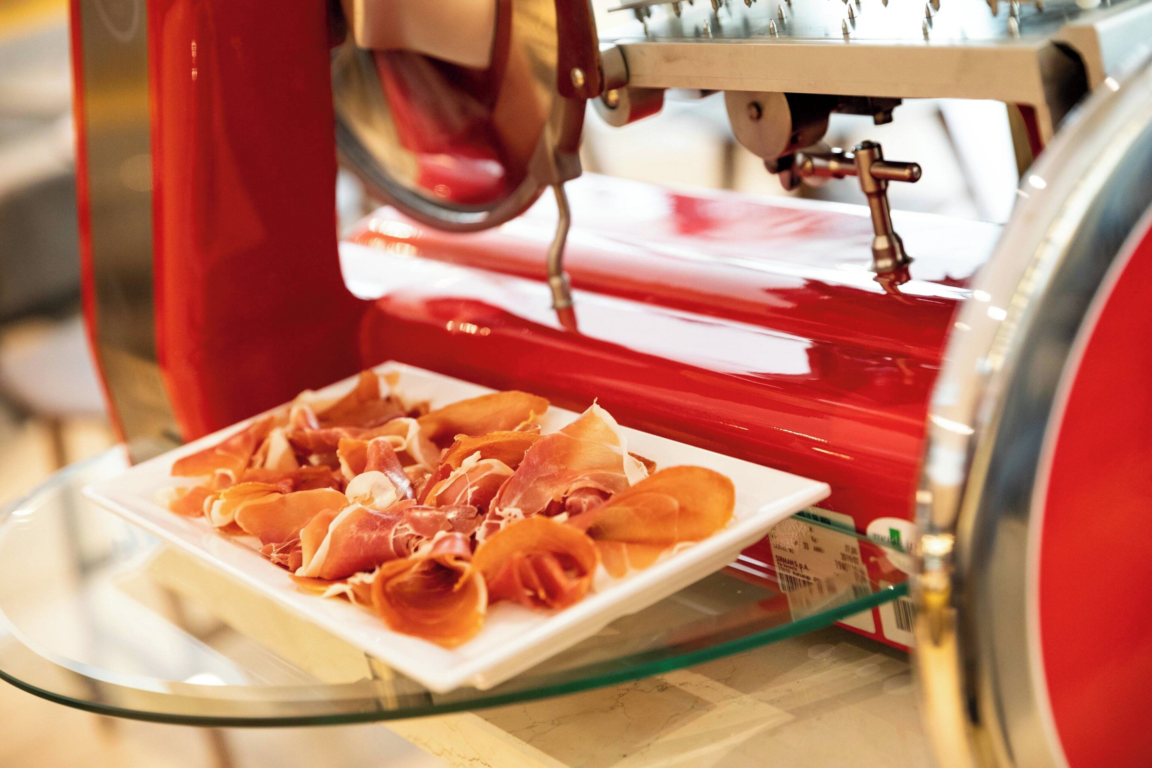 A red meat slicer with a plate of sliced meat in front of it.