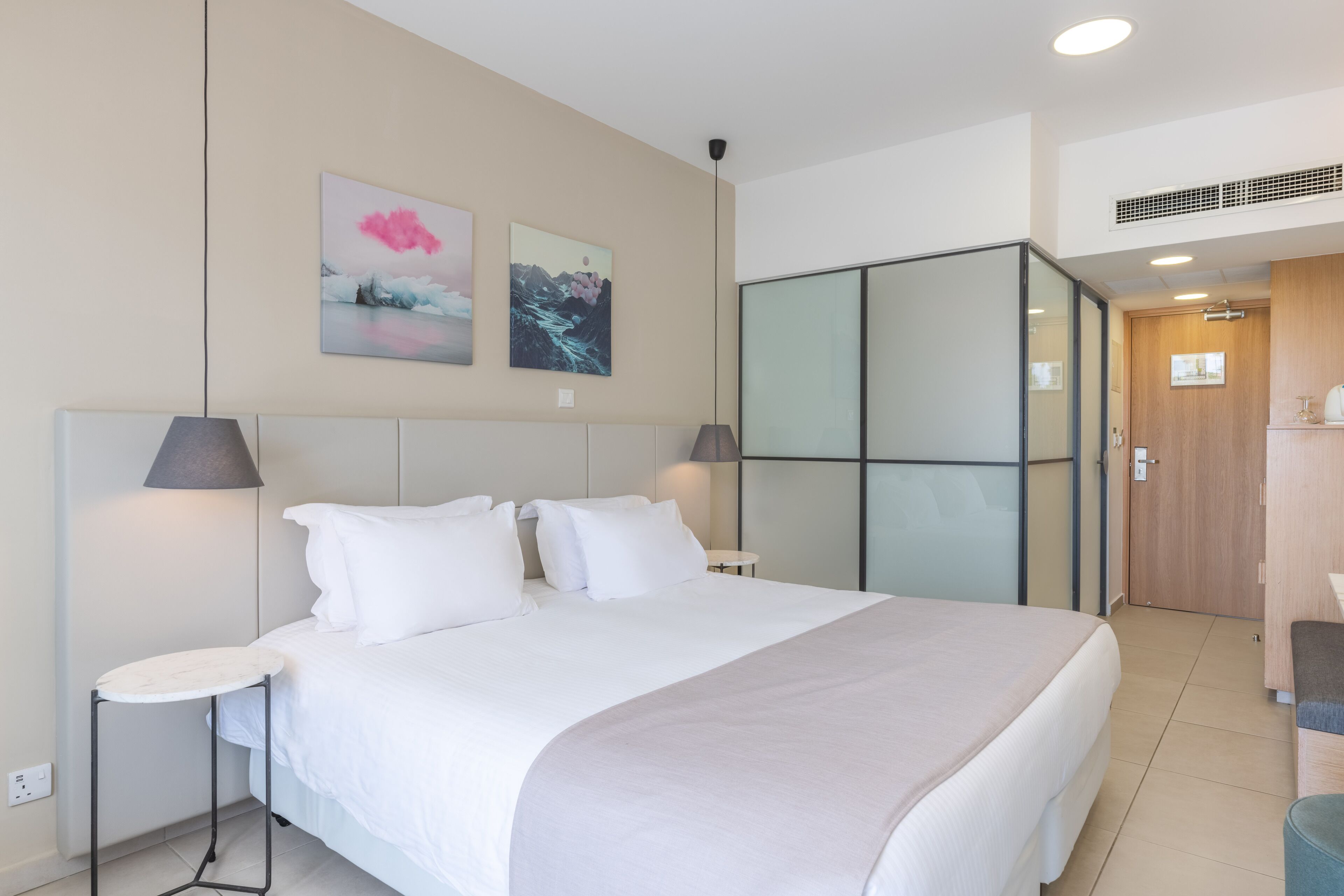 A modern hotel room with a large bed, bedside tables, and artwork on the walls.