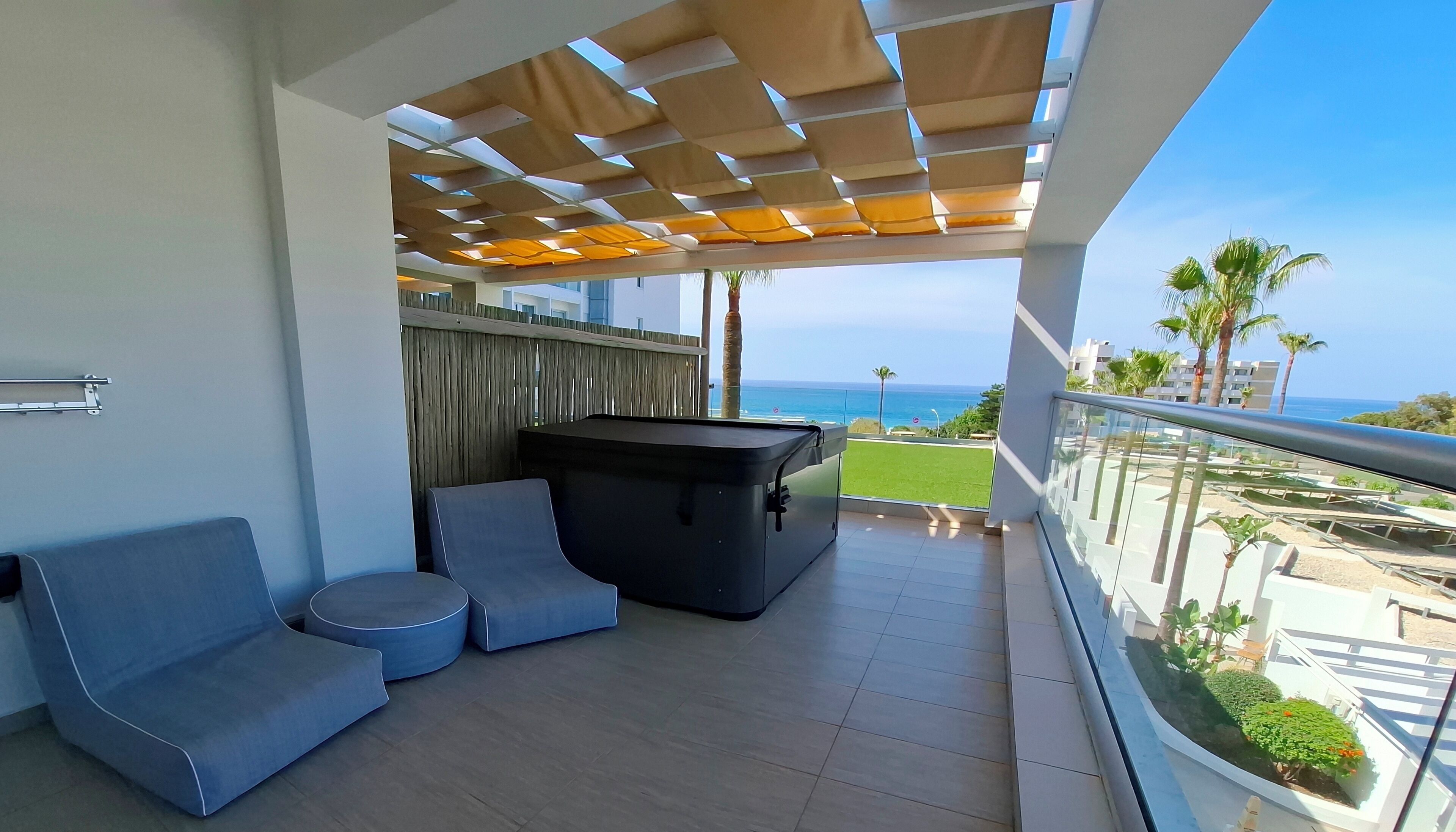 Un balcon aménagé avec un canapé, une petite table et un barbecue. Le balcon donne sur un espace verdoyant et un immeuble d’où l’on peut admirer la mer.
