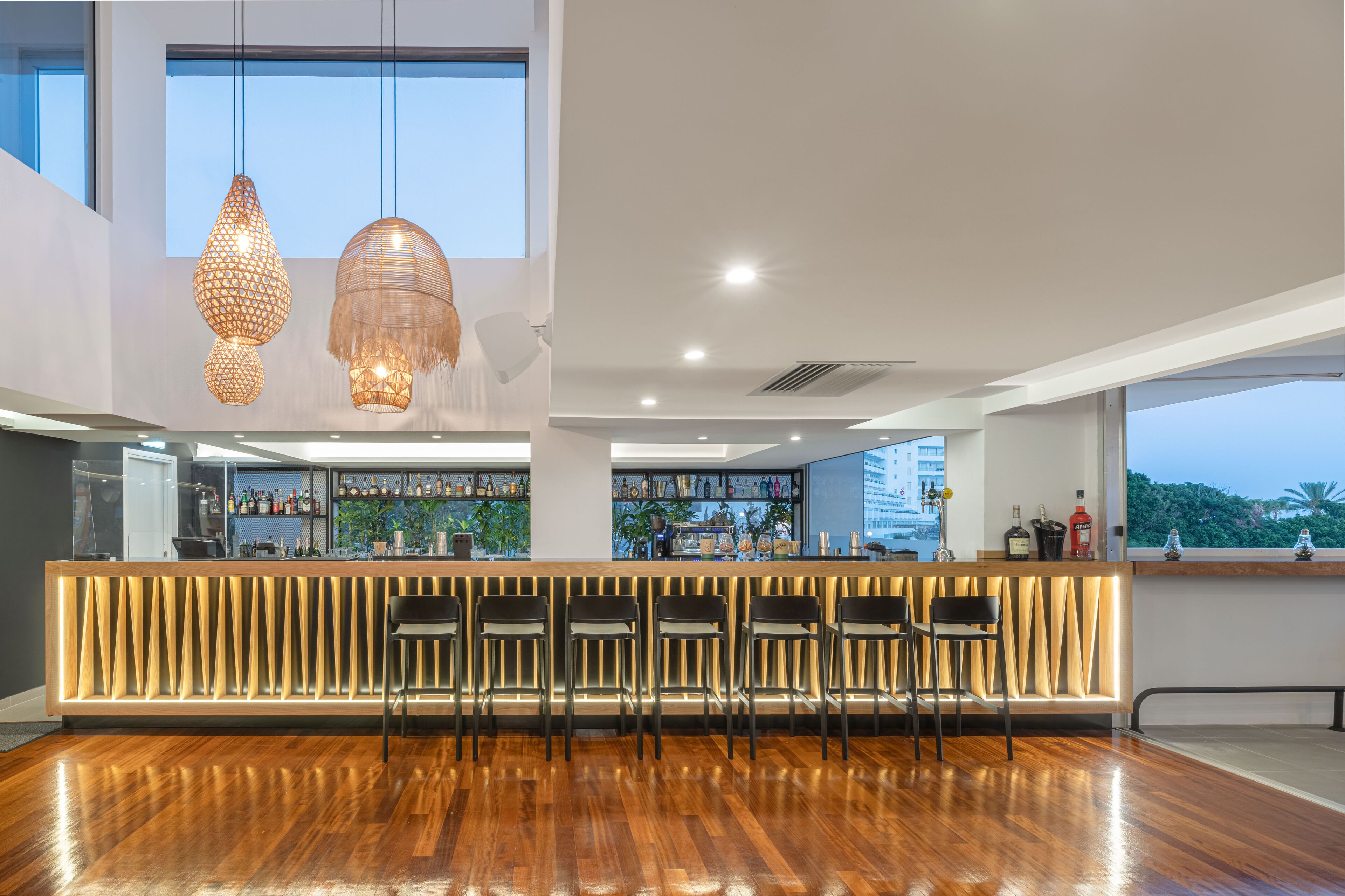 A modern bar area with wooden flooring, a bar counter, and several bar stools.