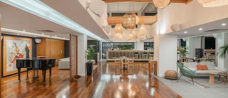 A spacious lobby with a grand piano, wooden flooring, and modern pendant lighting.