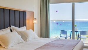 A hotel room with a large bed, a wooden headboard, and a view of the sea through large windows. - Napa Mermaid Hotel & Suites (Ayia Napa)