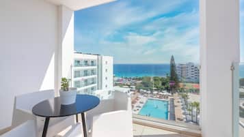 A balcony with a view of a pool and resort area, white chairs, and a small table.