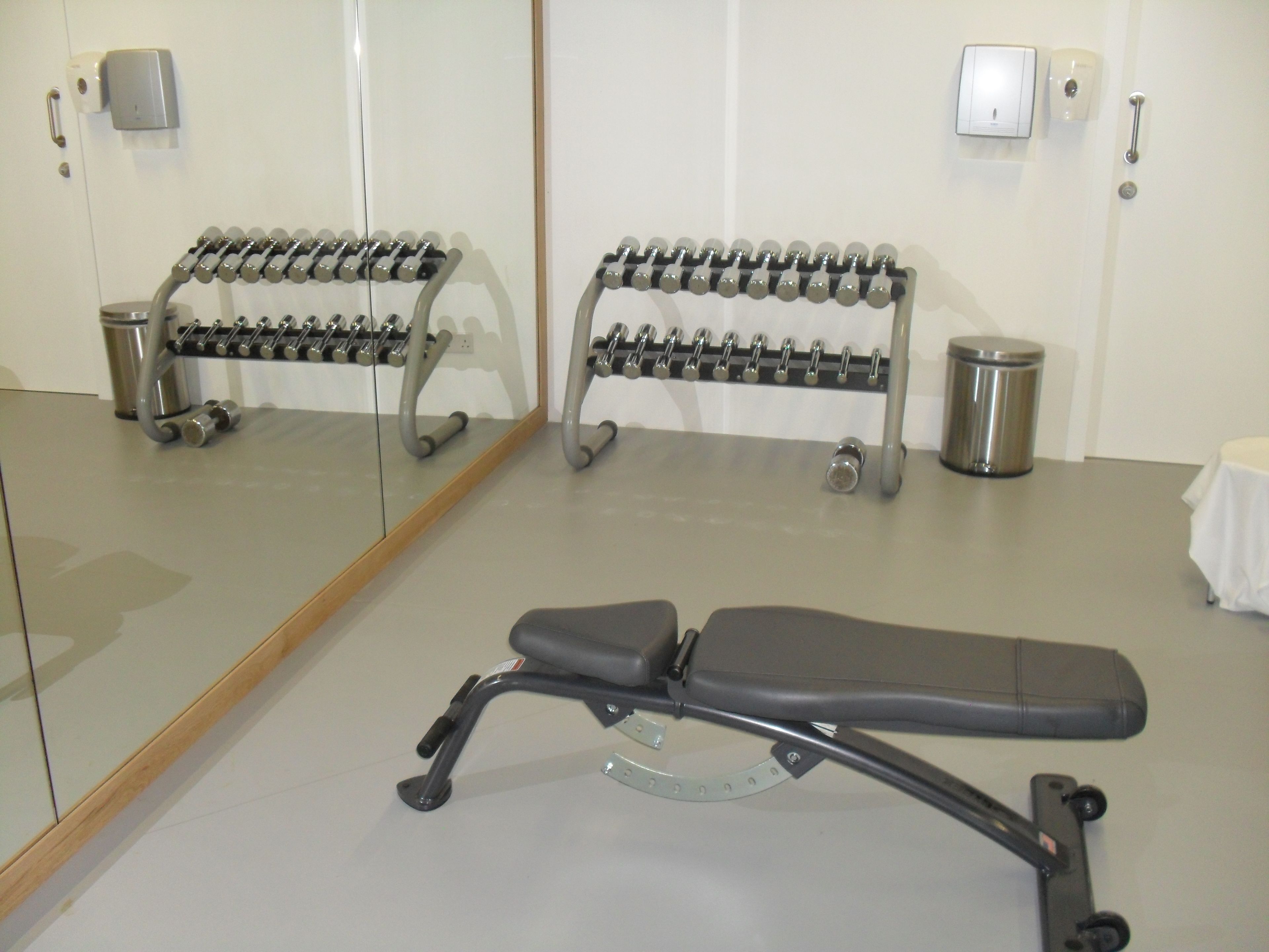 A gym with a mirrored wall, a bench, and a rack of dumbbells.