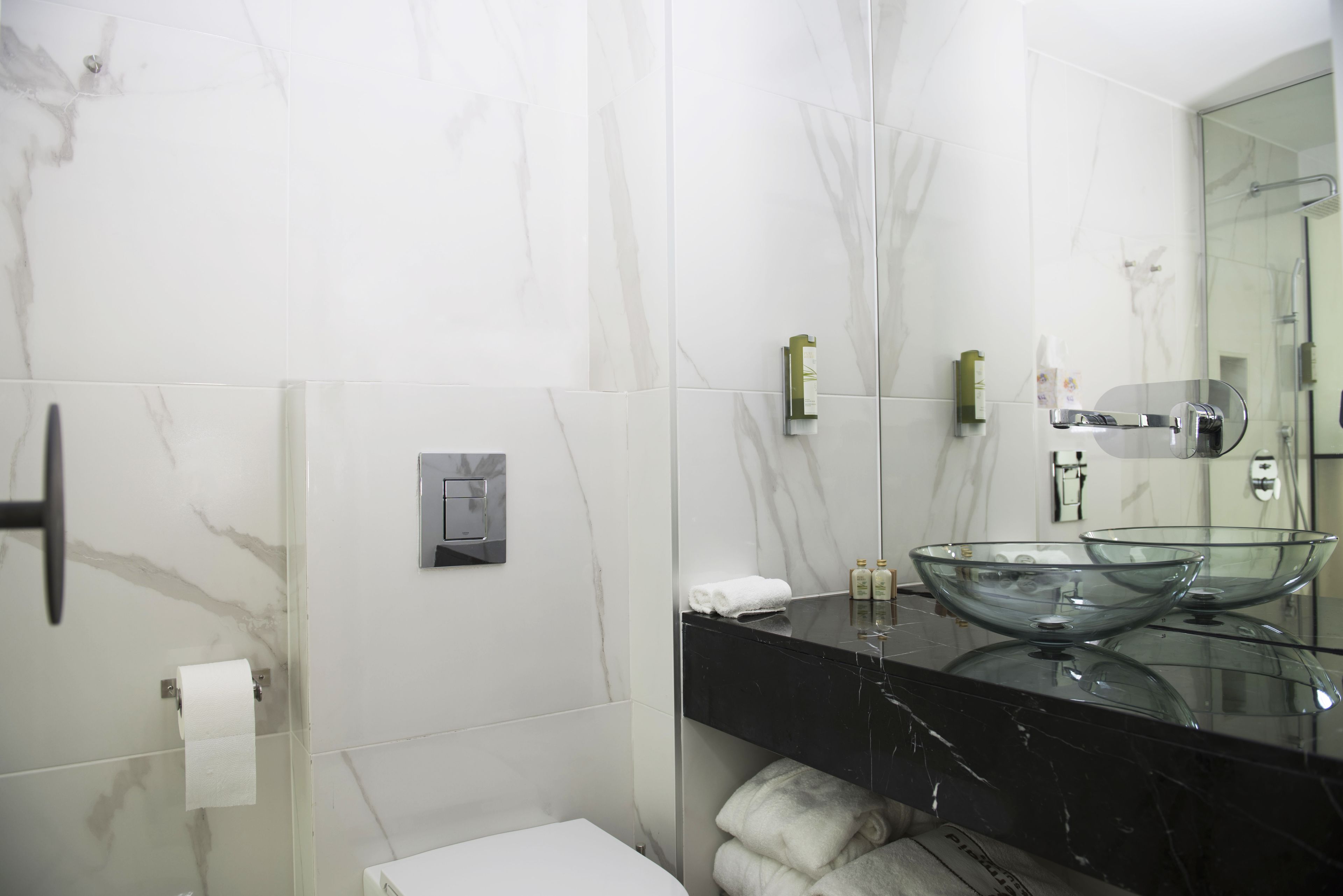 Un baño moderno con un lavabo de cristal, una encimera negra y un box de ducha de vidrio.
