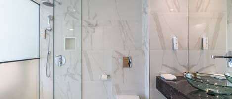 Un baño moderno con cabina de ducha de vidrio, inodoro blanco y lavamanos de vidrio sobre encimera negra.