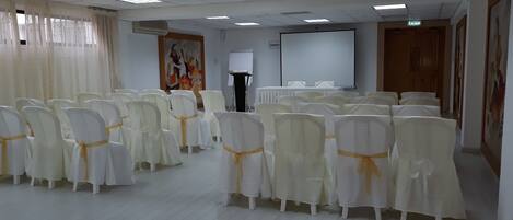 A conference room with rows of white chairs with yellow sashes, a whiteboard, and a projector screen.