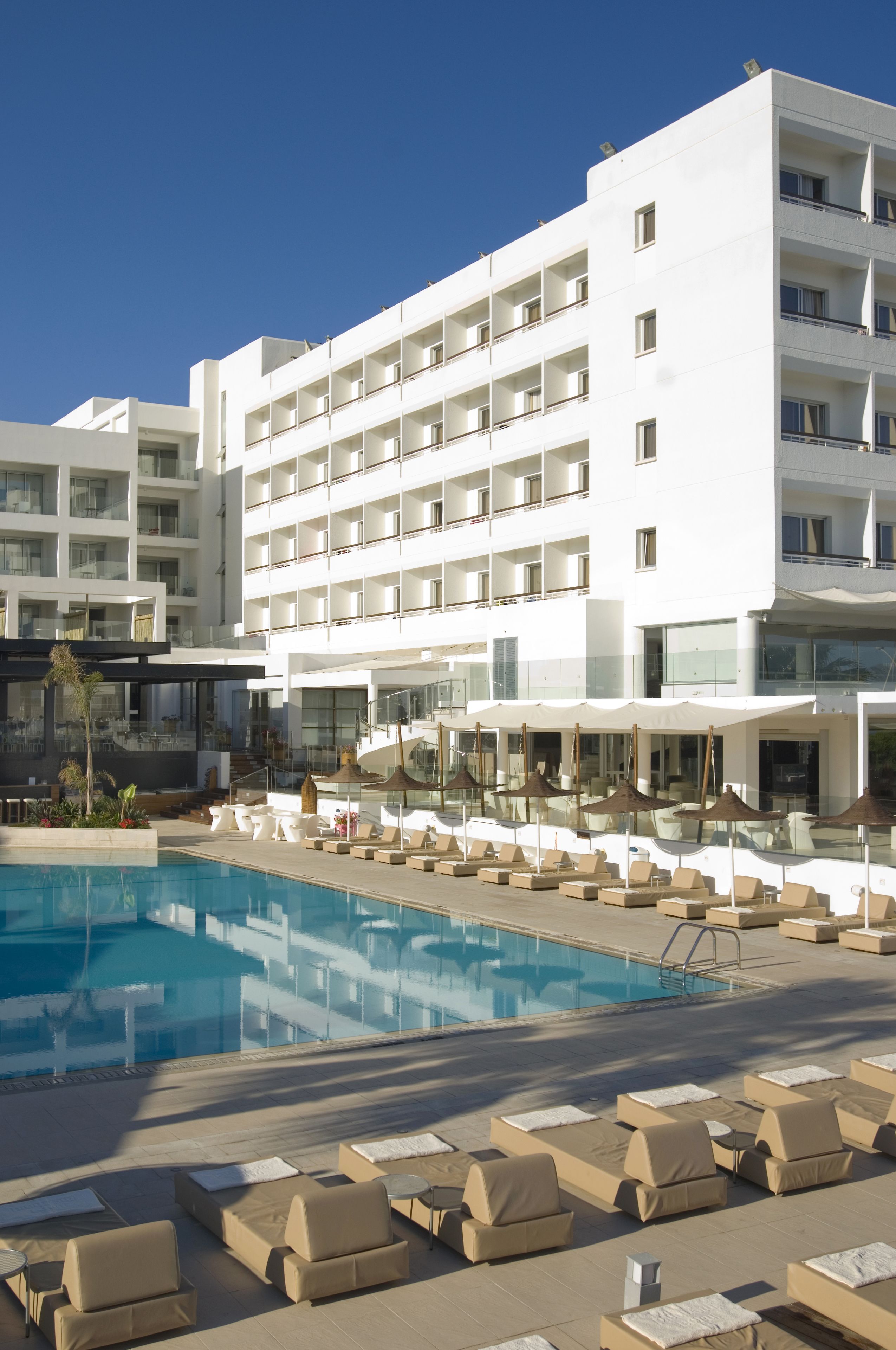Un hôtel moderne doté d’une piscine, de plusieurs balcons et de chaises longues.