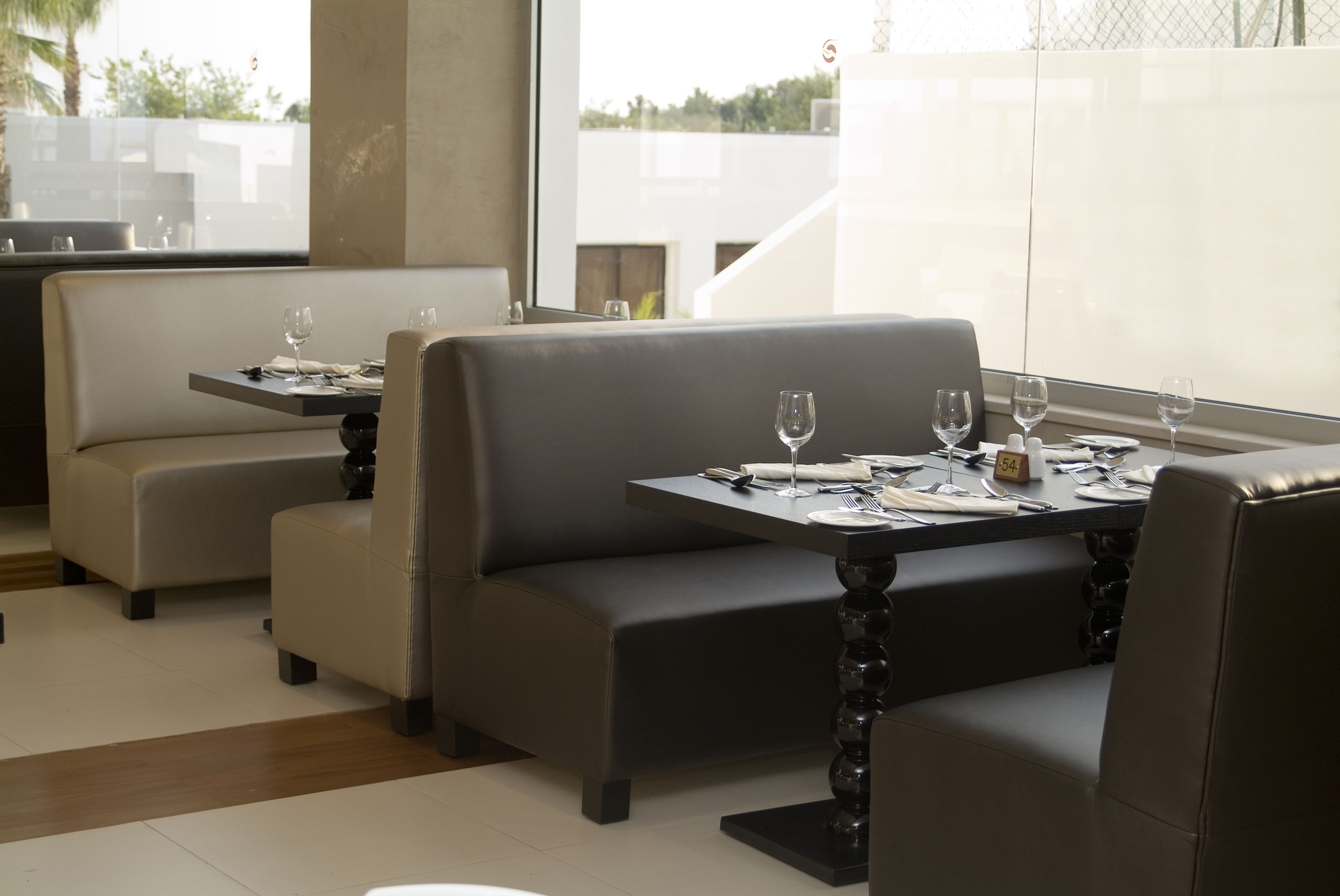 Un comedor moderno con asientos acolchados y mesas dispuestas para dos, con vistas al exterior.