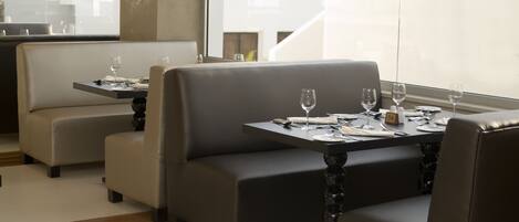 Un comedor moderno con asientos acolchados y mesas dispuestas para dos, con vistas al exterior.