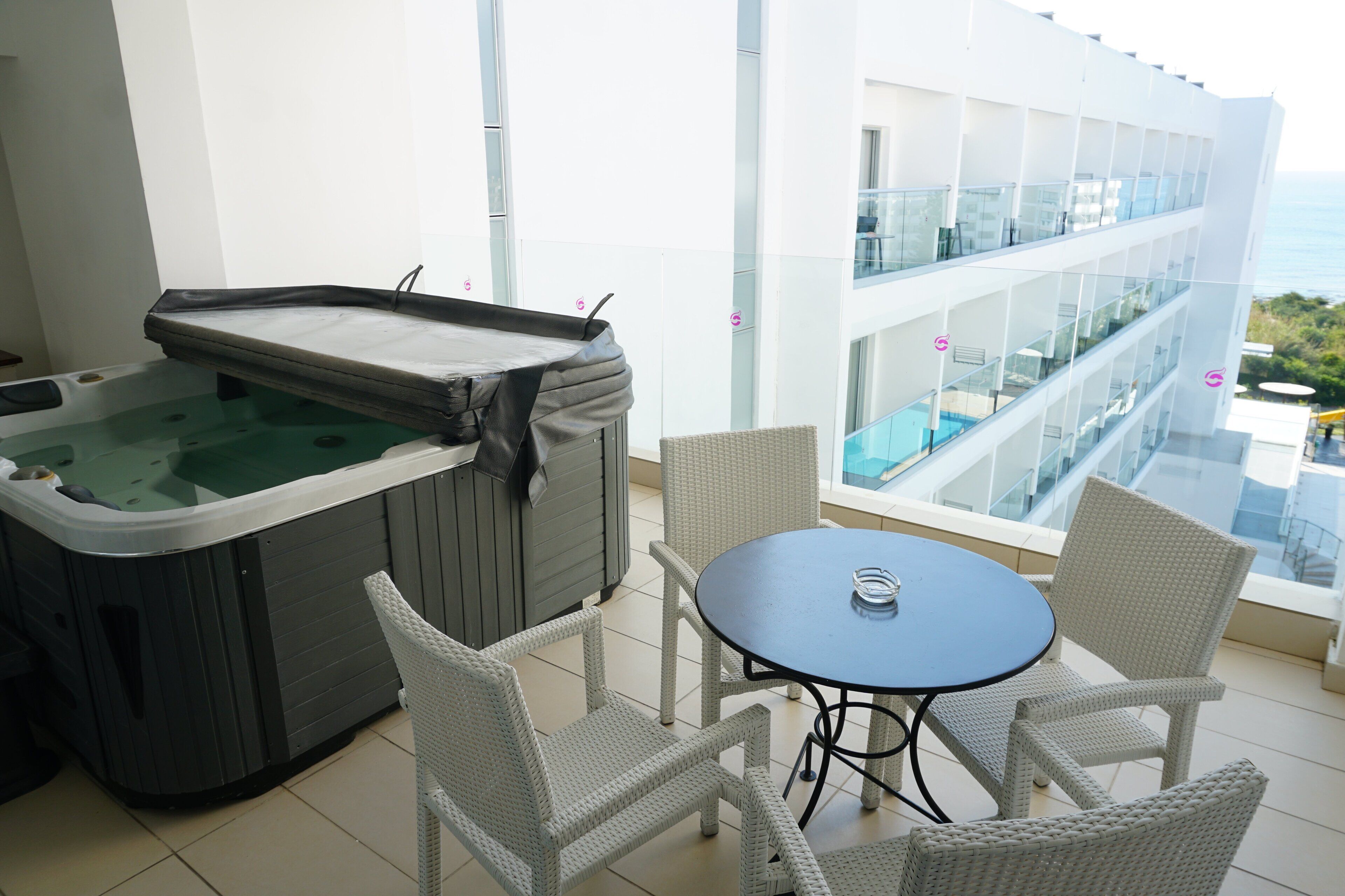 Ein Whirlpool mit Tisch und Stühlen auf einem Balkon mit Blick auf einen Pool und ein Gebäude.