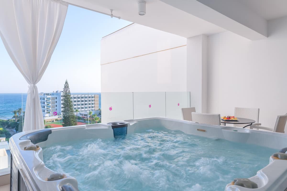 Un bain à remous avec vue sur l’océan, un balcon avec une table et des chaises, et un aménagement intérieur moderne.