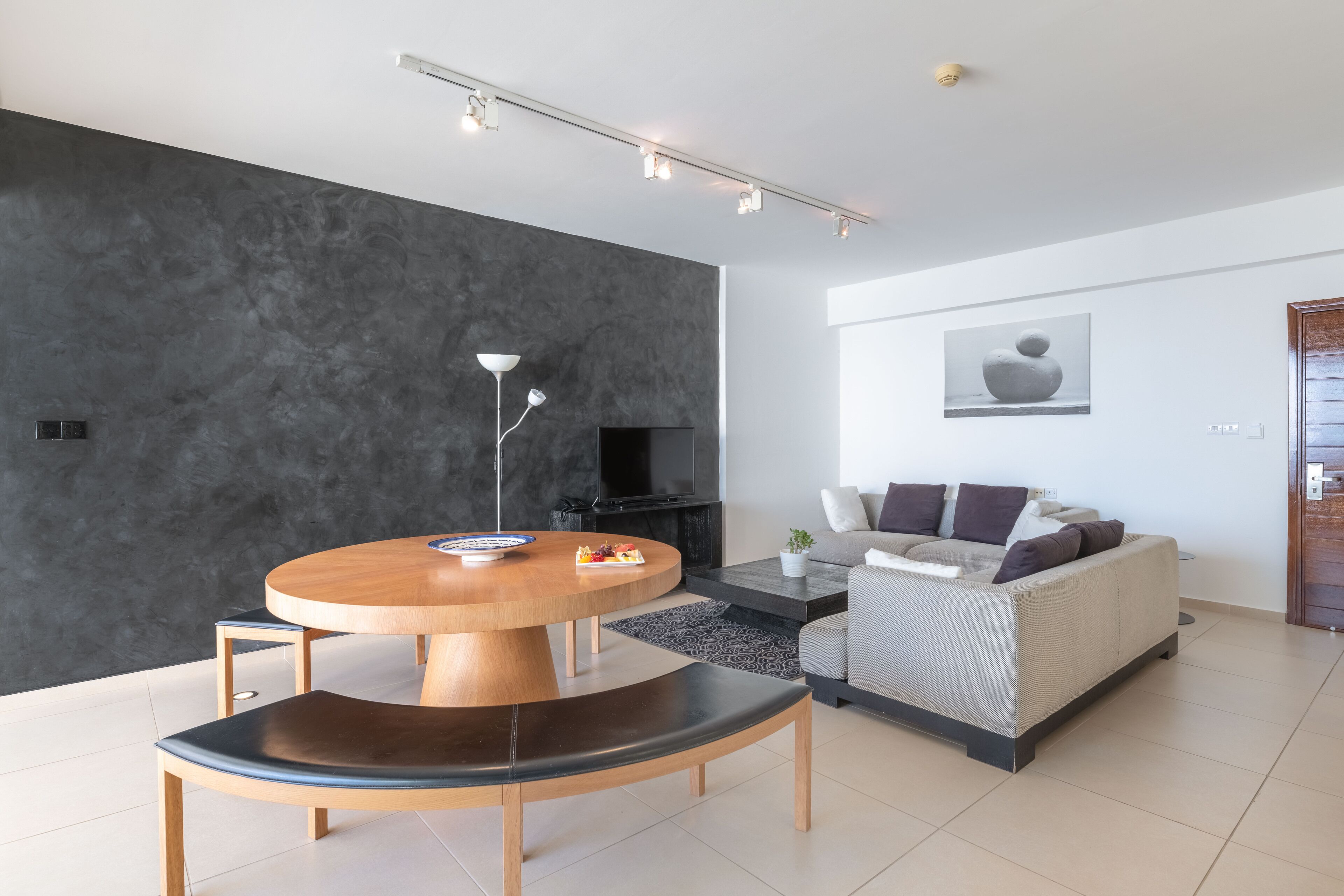 A modern living room with a round wooden dining table, a sofa, and a flat-screen TV.