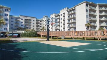 Un edificio residencial de varios pisos con balcones, una cancha de baloncesto y una terraza de madera.