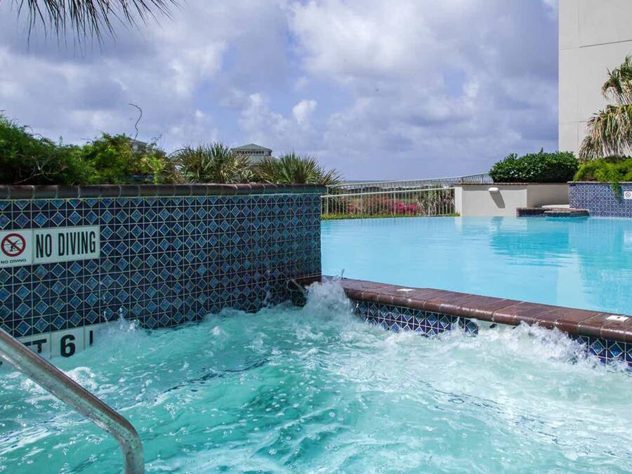 Piscina com placa de 'NÃO MERGULHAR', rodeada por um muro de azulejos e palmeiras.