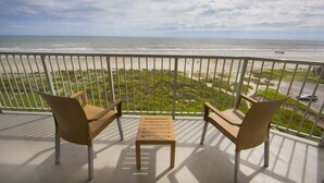 Ein Balkon mit zwei Stühlen und einem kleinen Tisch mit Blick auf einen Strand und das Meer.