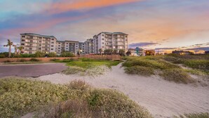 Ein Strandhotel mit mehreren Etagen und Balkonen, umgeben von Dünen und Vegetation.