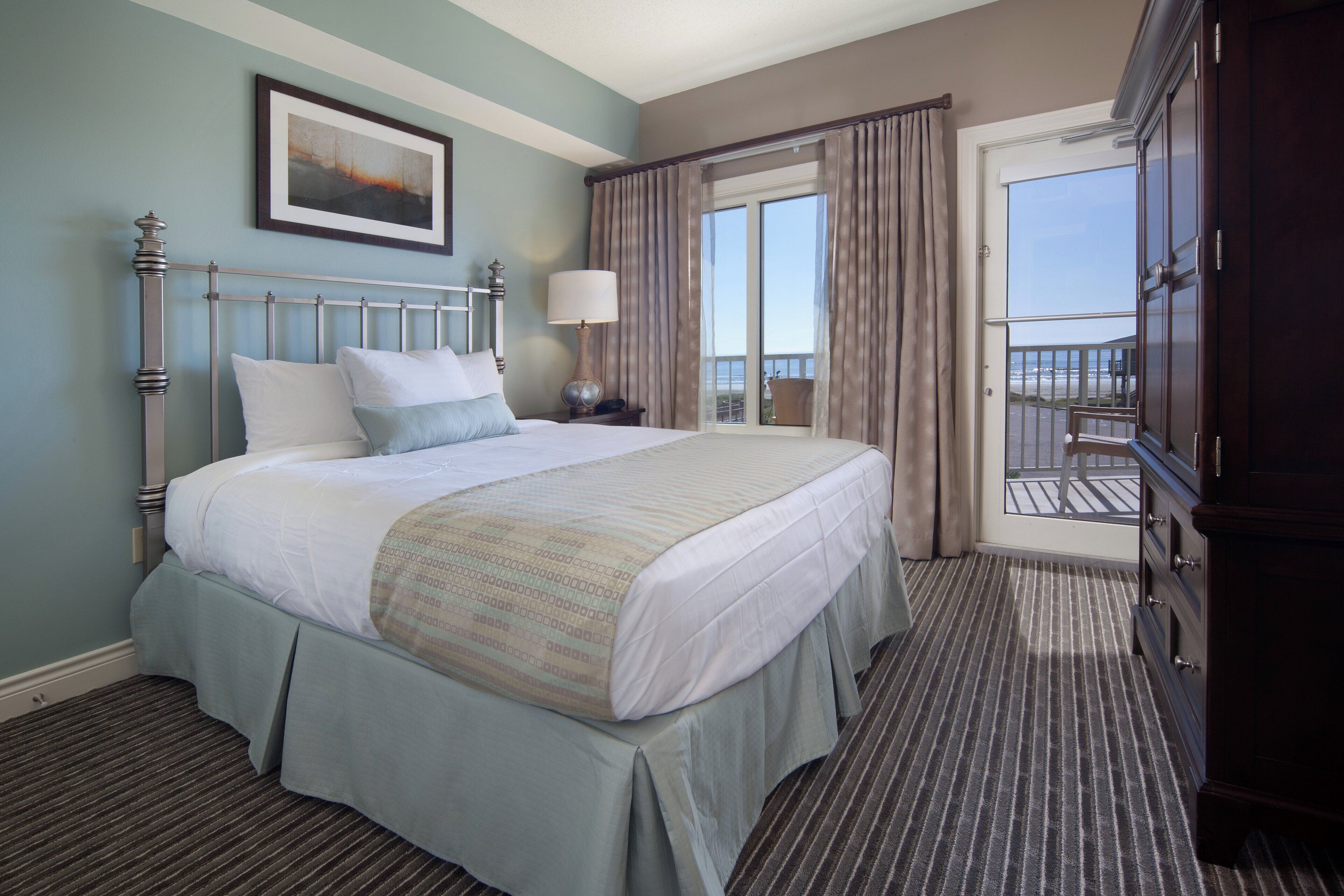 Habitación de hotel con cama, mesita de noche, lámpara, ventana con cortinas y vistas al exterior.
