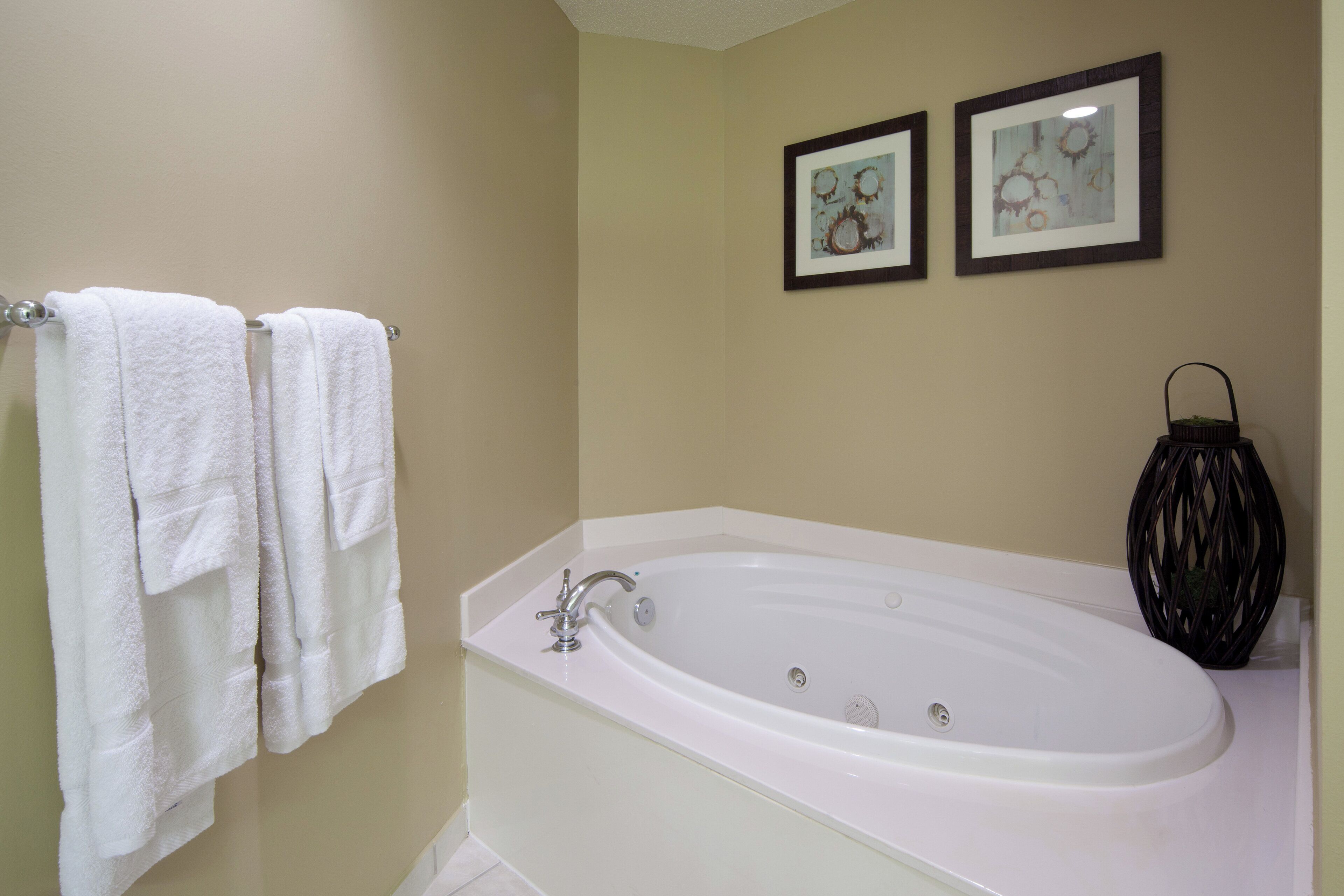 A bathroom with a white bathtub, a towel rack with two white towels, and two framed pictures on the wall.