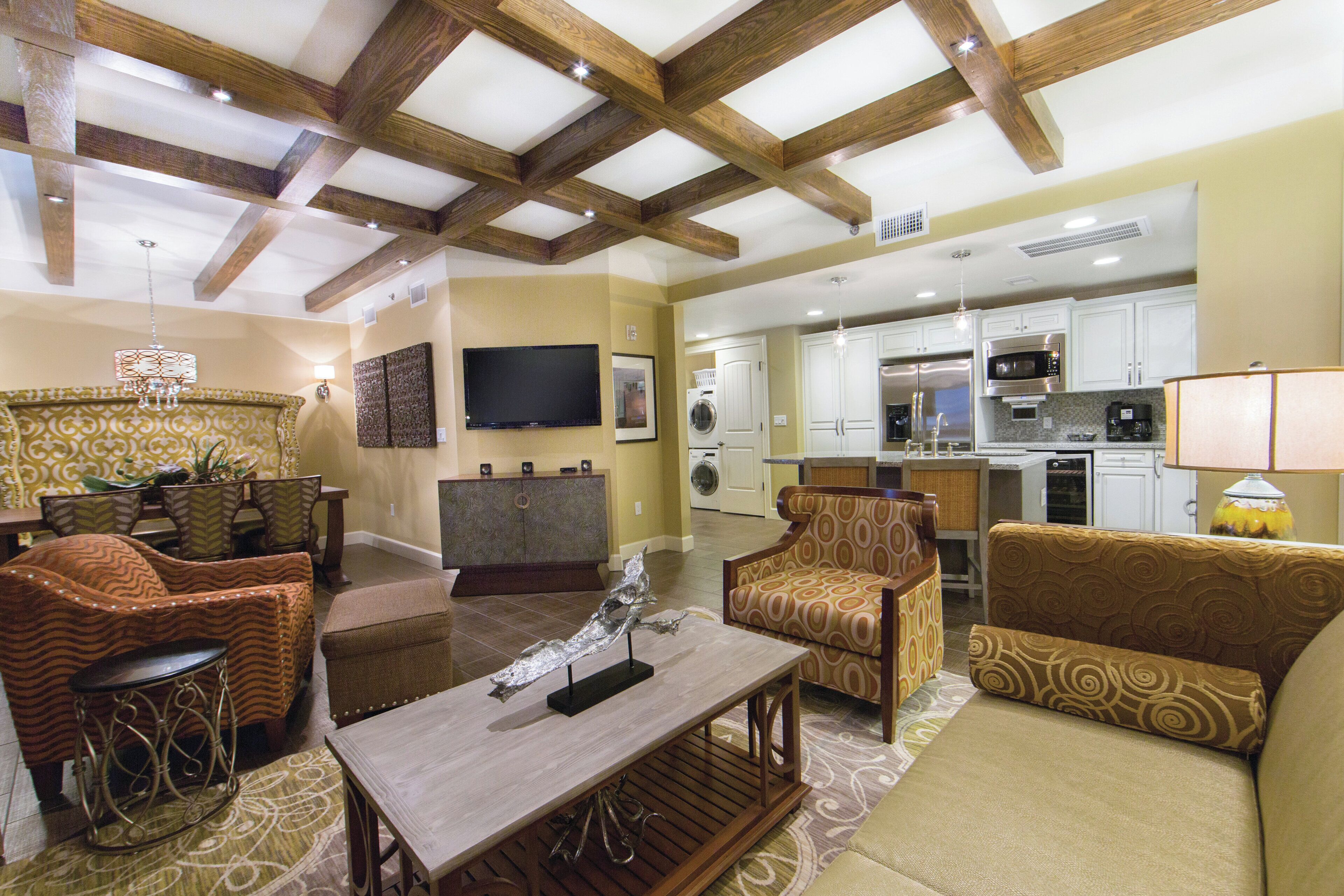 A spacious living area with a high ceiling, wooden beams, a dining set, a sofa, and a kitchen in the background.