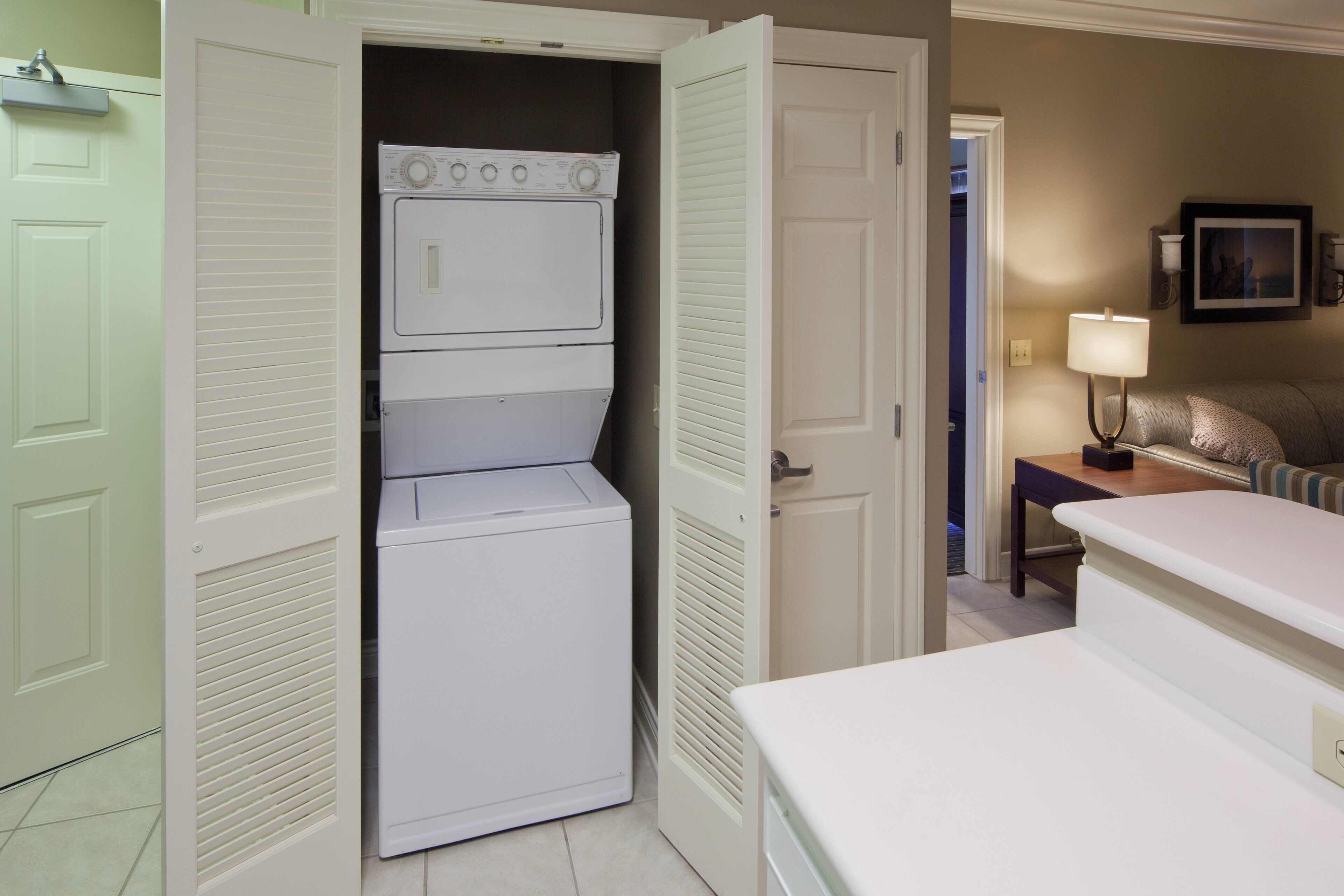 A compact laundry room with a washer and dryer, a small table with a lamp, and a couch in the adjacent living area.
