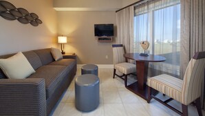 A modern living room with a sofa, two ottomans, a striped chair, a table, and a TV mounted on the wall. - Holiday Inn Club Vacations Galveston Beach Resort by IHG (Galveston)
