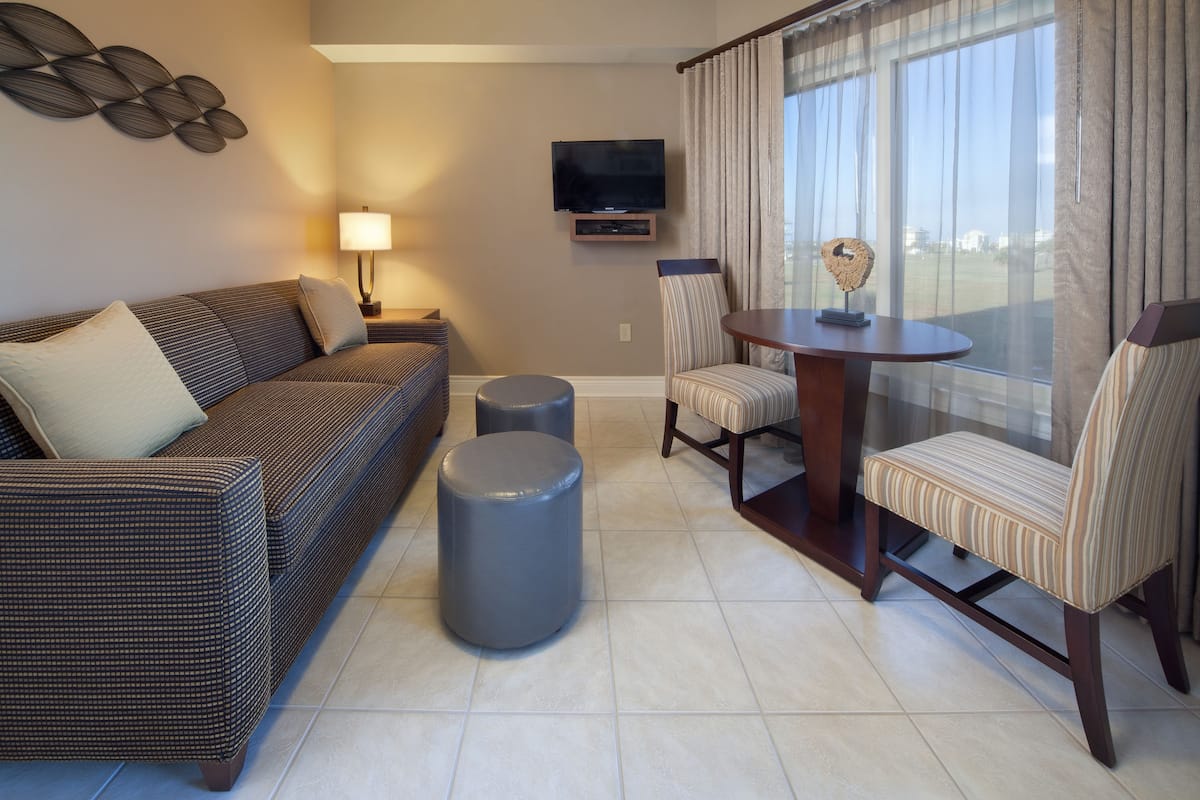 Un salon moderne comprenant un canapé, deux poufs, un fauteuil à rayures, une table et un téléviseur fixé au mur.