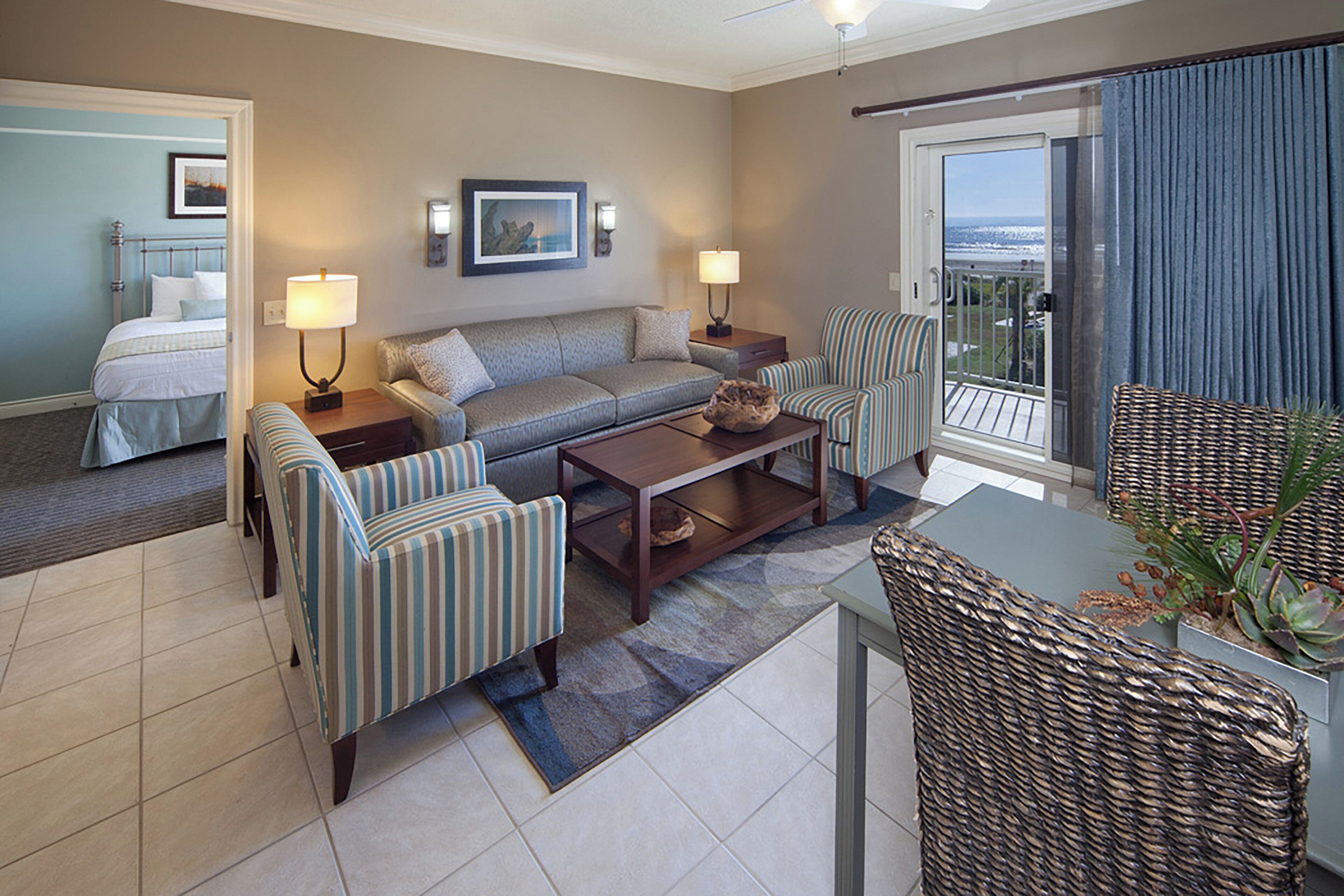 A hotel room with a bed, a sofa, two armchairs, a coffee table, and a balcony with a view.