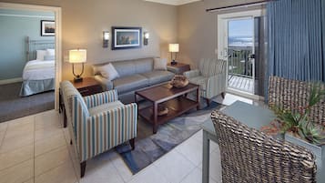 Habitación de hotel con cama, sofá, dos sillones, una mesita de centro y balcón con vistas.