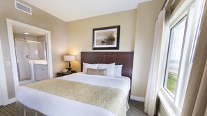 A hotel room with a large bed, a bedside table with a lamp, a framed picture on the wall, and a window with curtains. - Holiday Inn Club Vacations Galveston Beach Resort by IHG (Galveston)