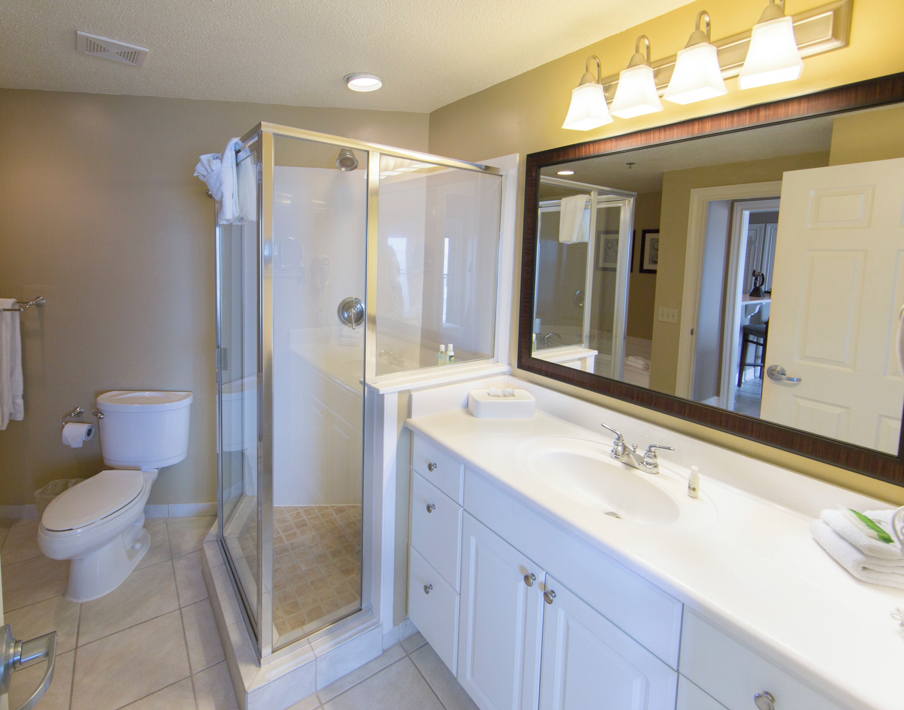 A bathroom with a glass-enclosed shower, a toilet, a sink with a mirror above it, and a towel rack.