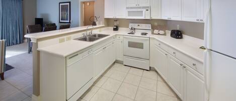 Una cocina moderna con armarios blancos, microondas integrado, estufa y refrigerador.