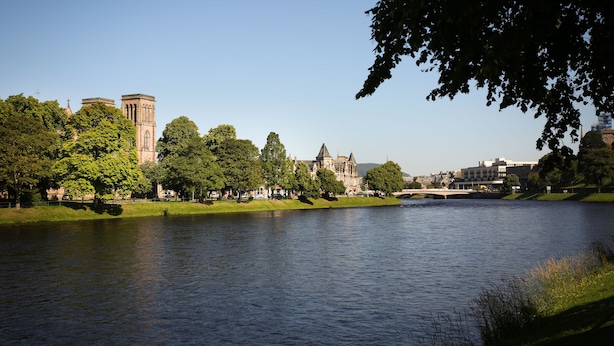 A river with a bridge, trees, and historic buildings in the background.
