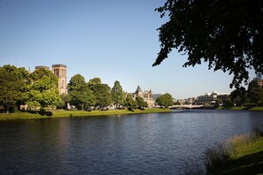 Un río con un puente, árboles y edificios históricos al fondo.