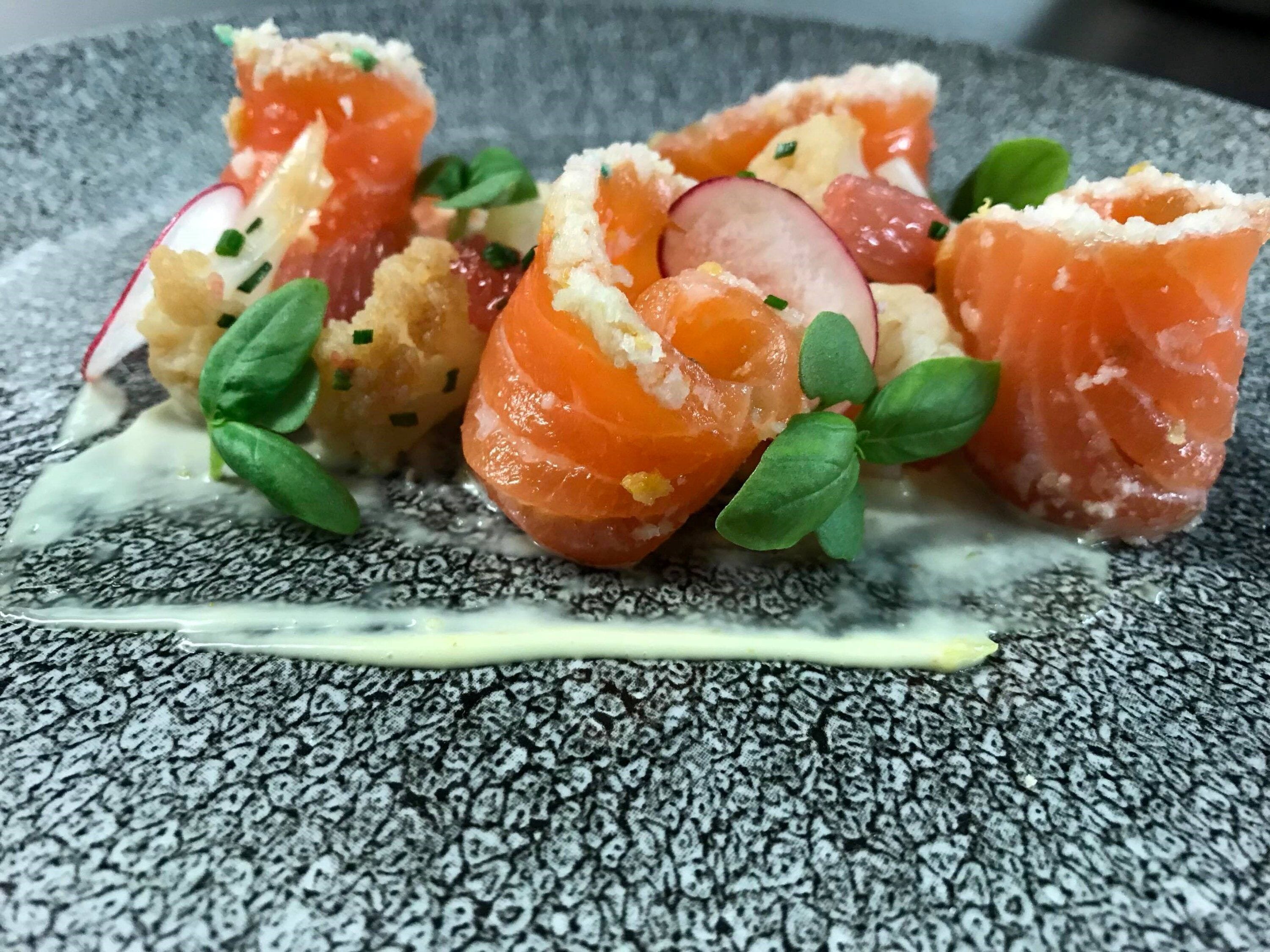 A dish with salmon, radishes, and greens on a textured plate.