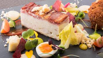 Ett urval av olika matvaror presenterade på en skifferbricka, inklusive en bit kött med krispig yta, ett kokt ägg samt olika grönsaker och garneringar.